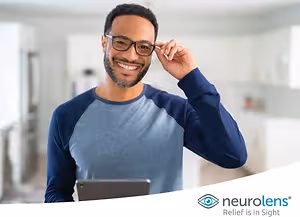 A man with glasses smiling in a room with a tablet in his hand, the brand name Neurolens is on the bottom right.