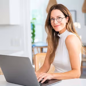 A woman with glasses is working on her laptop in a room