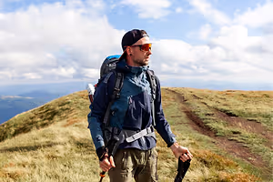 A man hiking in a mountain with a clear sky and clouds in the background