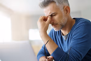 Senior man rubbing his eyes while looking at his laptop screen in a room