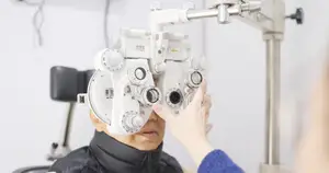 An elderly man is getting his eyes checked by a medical professional using an ophthalmoscope