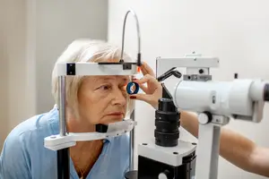 An elderly woman examining her eye with an eye exam machine