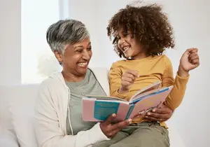 An older woman and a young girl are sitting on a couch and reading a book together.