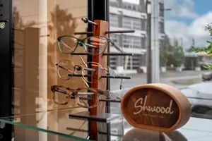 Multiple pairs of Shwood brand glasses are displayed on a glass stand in front of a shop window