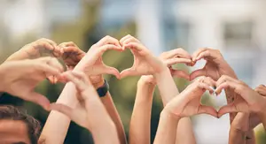 Many people forming a heart shape with their hands in a group