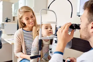 A young girl is having her eyes checked by an optician in a room with white walls.