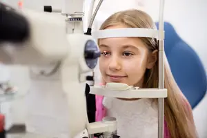 A young girl with long blonde hair is having her eyes examined by an ophthalmologist in an eye clinic.