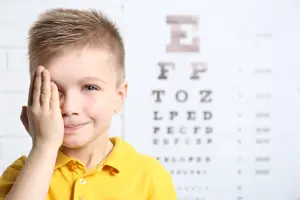 A young boy wearing a yellow shirt and standing in front of an eye chart with blurry letters