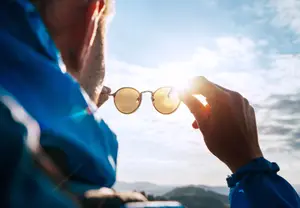 A man wearing a blue jacket and glasses is looking at the sun through his sunglasses.