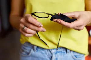 A woman is holding a pair of glasses in her hands, possibly adjusting them.