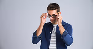 A man in a blue shirt adjusting his glasses while holding a pencil