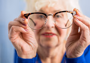 A senior woman is trying to see something with her glasses in her hands