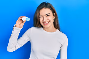 A woman smiling and holding a bottle of eye drops in her hand