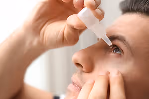 A man is administering eye drops to his eye