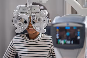 A young woman wearing a striped shirt is getting her eyes examined with an eye exam machine.