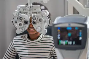A young woman wearing a striped shirt is getting her eyes examined with an eye exam machine.