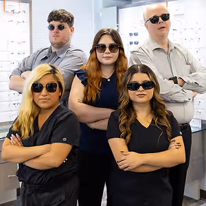 Five people in sunglasses pose for a photo in a room with glass walls displaying sunglasses