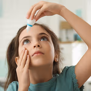 A young girl is administering eye drops to her eye.