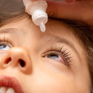 A young girl has an eyedropper held by another person to her eye
