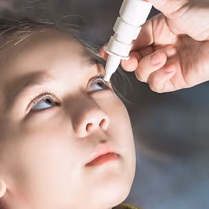 A person administering eye drops to a child