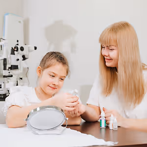 A young girl and a woman are smiling and seem to be looking at a bottle in front of them, probably in an optometrist's office.