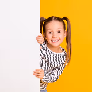 A smiling girl with pigtails holding a white board in front of a yellow background