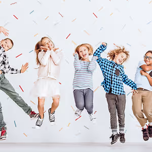 Five children jumping in the air in front of a white background with multicolored confetti