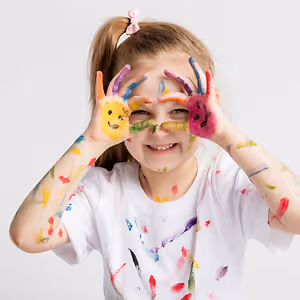 A young girl with colorful paint on her hands and face, smiling and posing for a picture.