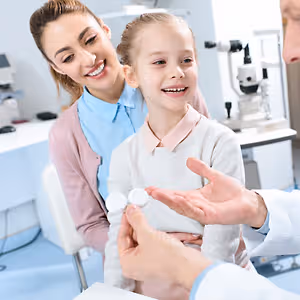 A doctor showing a girl and her mother two white contact lenses