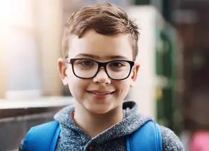 A smiling young boy with glasses and a backpack