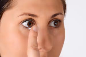 A woman is trying to insert a contact lens into her eye.