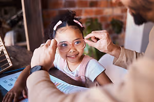A man is adjusting a young girl's glasses at a desk