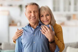 An older couple smiling at the camera, standing in a living room