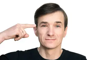 Close up of a man with his hand on his ear and a ring on his finger smiling