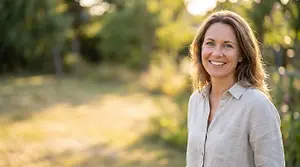 A smiling woman stands in a park on a sunny day, surrounded by greenery.