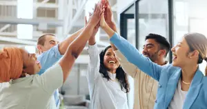 A group of smiling people are giving a high five to each other in an indoor area.