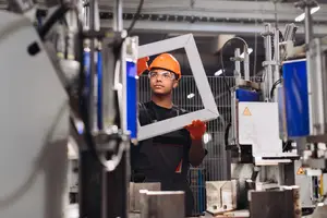 A young man is working in a factory holding a white frame
