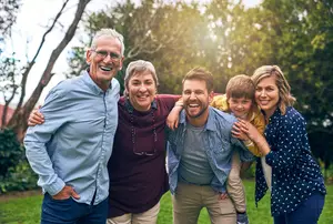A group of five people smiling and standing close to each other in a park