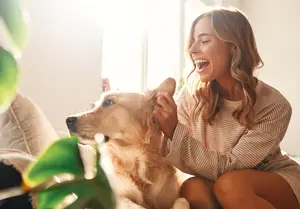 Woman sitting on a couch with her dog, both of them looking joyful and smiling