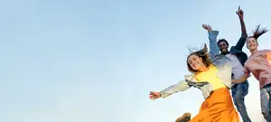 Four people jumping in the air with smiles on their faces under a clear blue sky