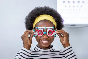 A young girl wearing glasses is smiling while holding a pair of eye glasses
