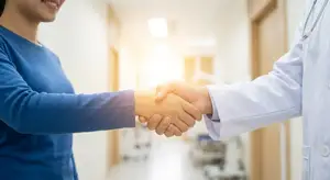 A doctor and patient shaking hands in a hospital hallway