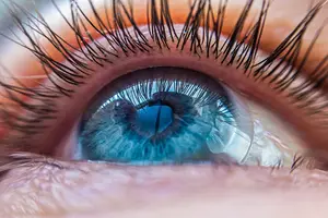 A close-up view of a person's blue eye with long lashes and a slightly open mouth.