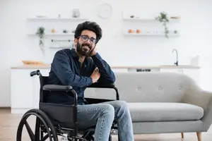 A man sitting in a wheelchair in a living room with a couch, smiling, and posing for a photo.