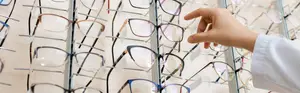 A hand is holding a pair of glasses in a display case with many other pairs of glasses