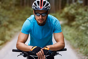 A man wearing a helmet and sunglasses is riding a bicycle on a concrete road with green plants on both sides.