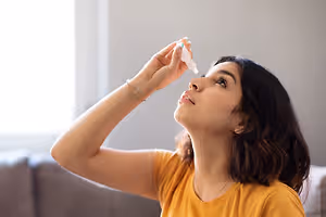 A woman is using eye drops in a room