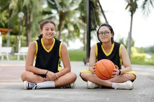 Two women sitting on the ground with a basketball