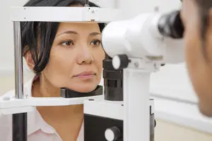 A woman is looking into an ophthalmoscope while an optician examines her eye.