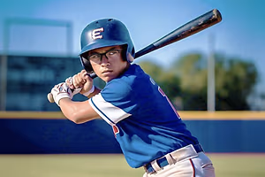 A baseball player in a blue jersey with the letter E on his helmet, holding a baseball bat and getting ready to hit the ball